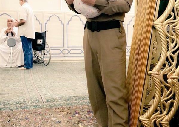 صورة لعسكري يحمل طفلاً بالمسجد النبوي كي يتمكن والده من الصلاة