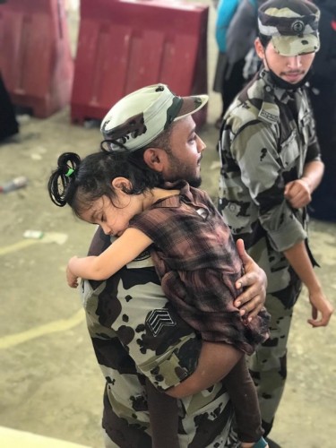 رجل أمن يحمل طفلة خلال قيام والدتها برمي الجمرة الصغرى