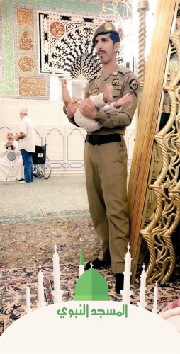 صورة لعسكري يحمل طفلاً بالمسجد النبوي كي يتمكن والده من الصلاة